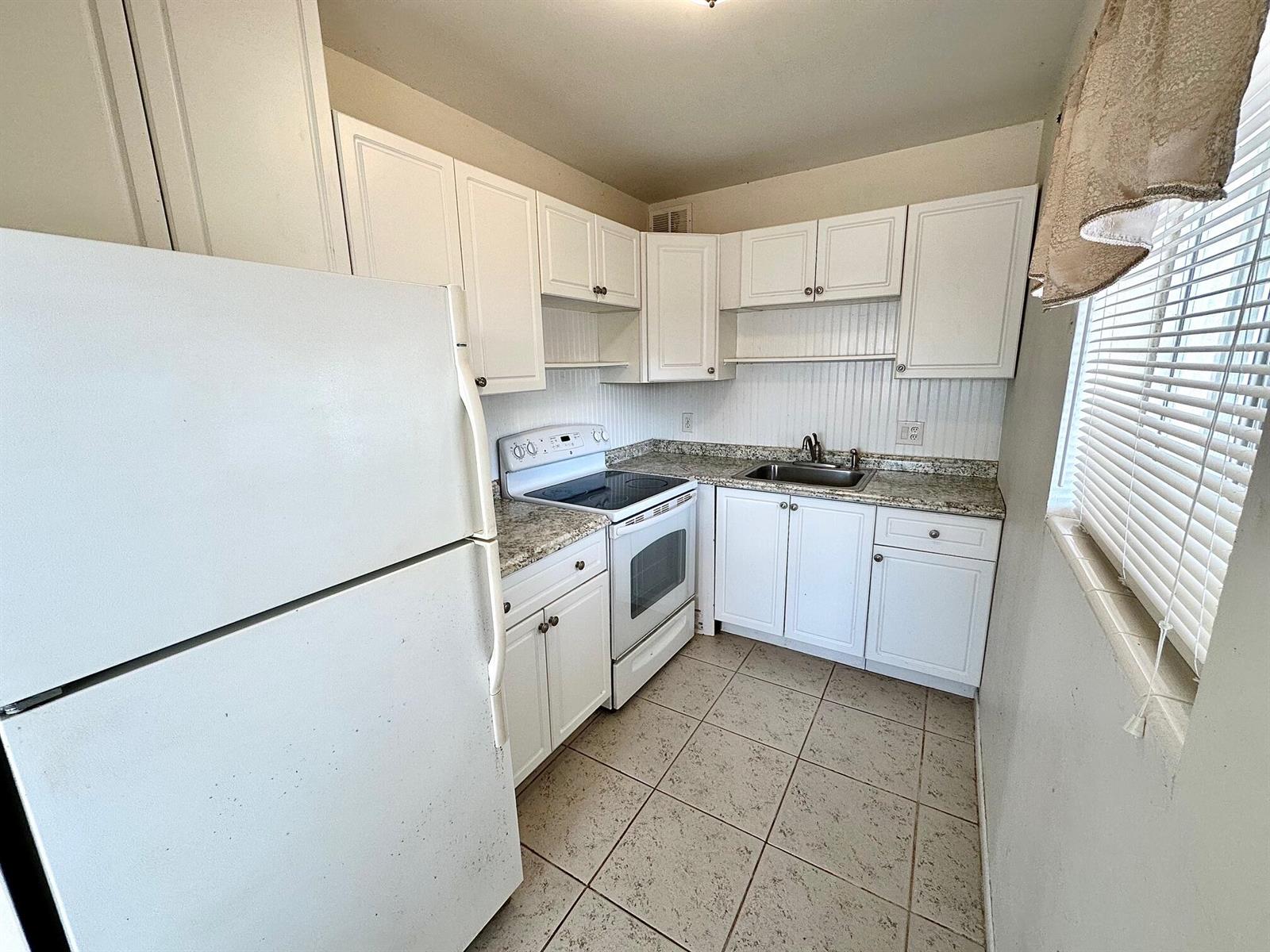 A small kitchen features white cabinets, a white refrigerator, a stove, and tiled flooring — 2880 Lake Osborne Drive # 210, FL 33461, FL