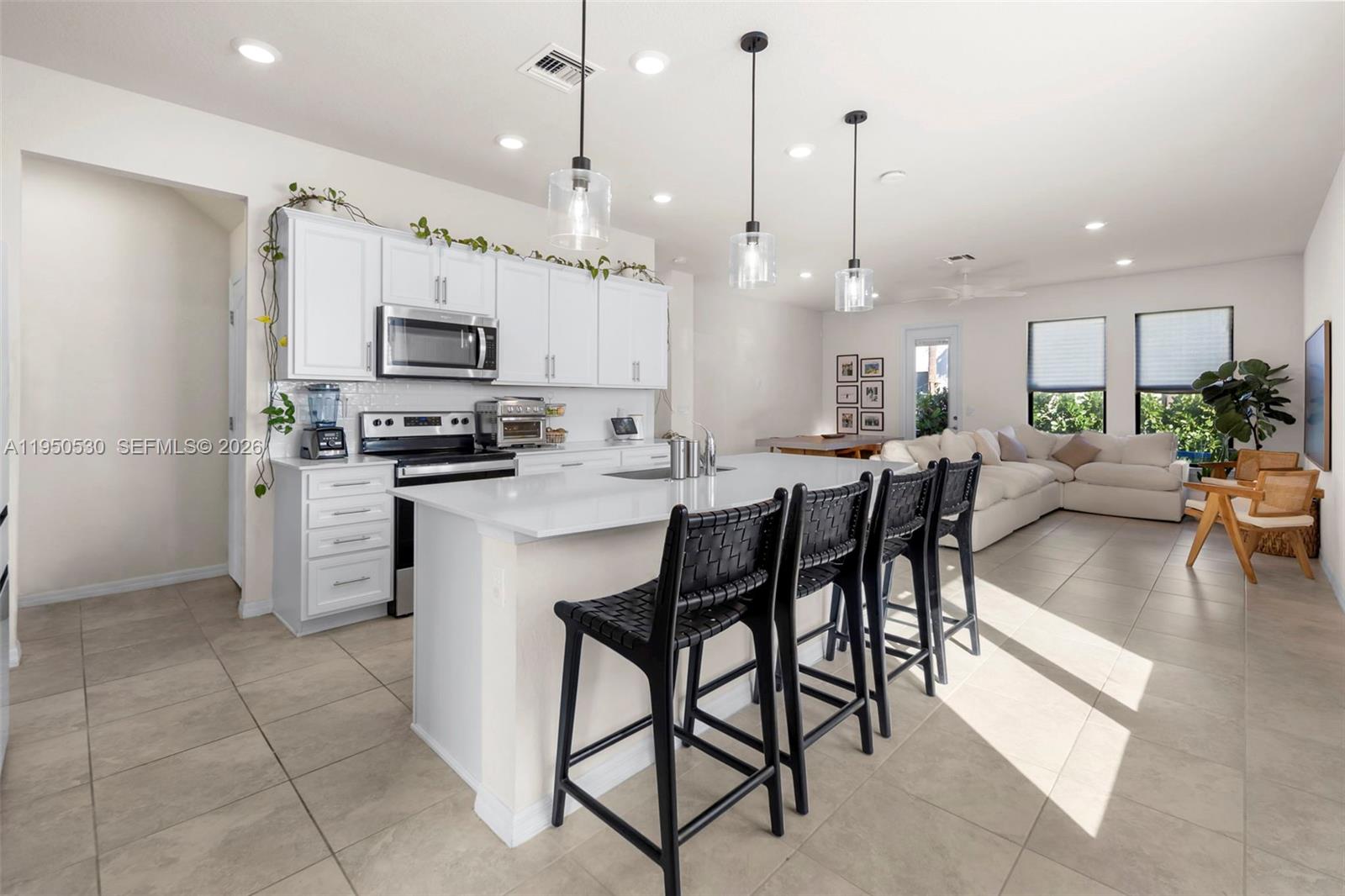A modern kitchen with white cabinets, a large island, and black bar stools — 2121 S Appleton Cir S, Oakland Park FL 33309, OAKLAND PARK, FL