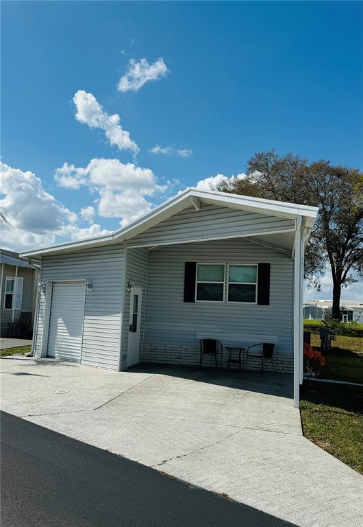 A light gray mobile home features a covered carport, a roll-up door, and a small patio — 627 ARNOLD PALMER DRIVE, DAVENPORT, FL
