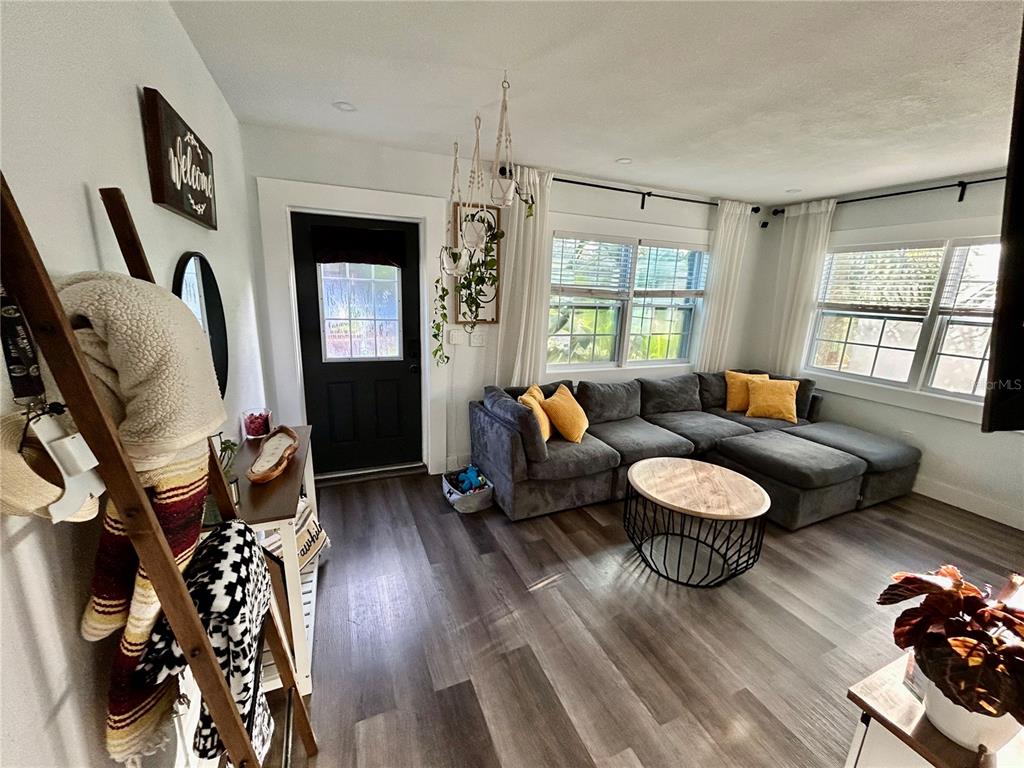 A living room features a grey sectional sofa, wood-look flooring, and a black front door — 3550 2ND AVENUE S, ST PETERSBURG, FL