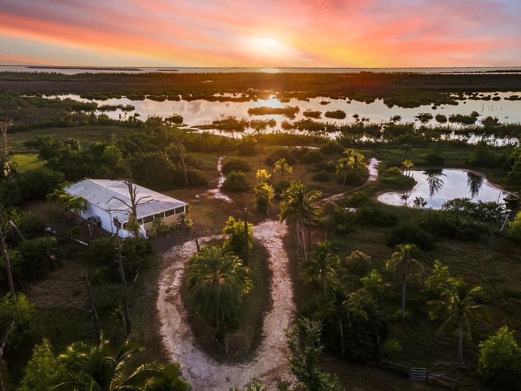 An aerial view of a house surrounded by palm trees, wetlands, and a sunset horizon — 5209 WESTERN DRIVE, ST JAMES CITY, FL