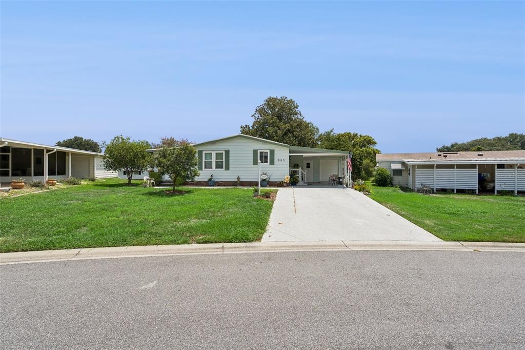 A light-colored single-story house with a driveway and carport sits on a grassy lot — 903 OLEANDER STREET, LADY LAKE, FL