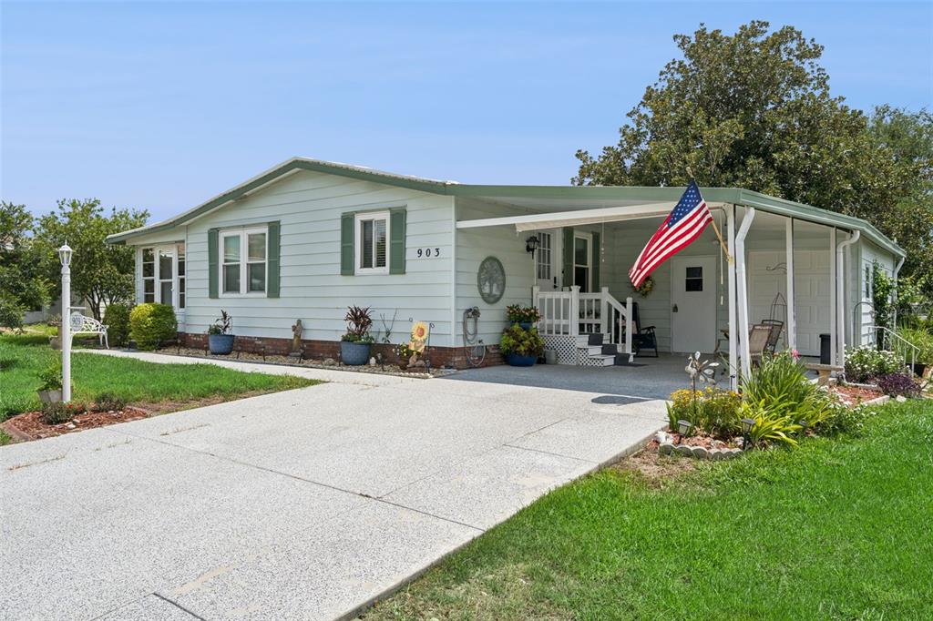 A light green single-story house with a carport, front porch, and an American flag — 903 OLEANDER STREET, LADY LAKE, FL