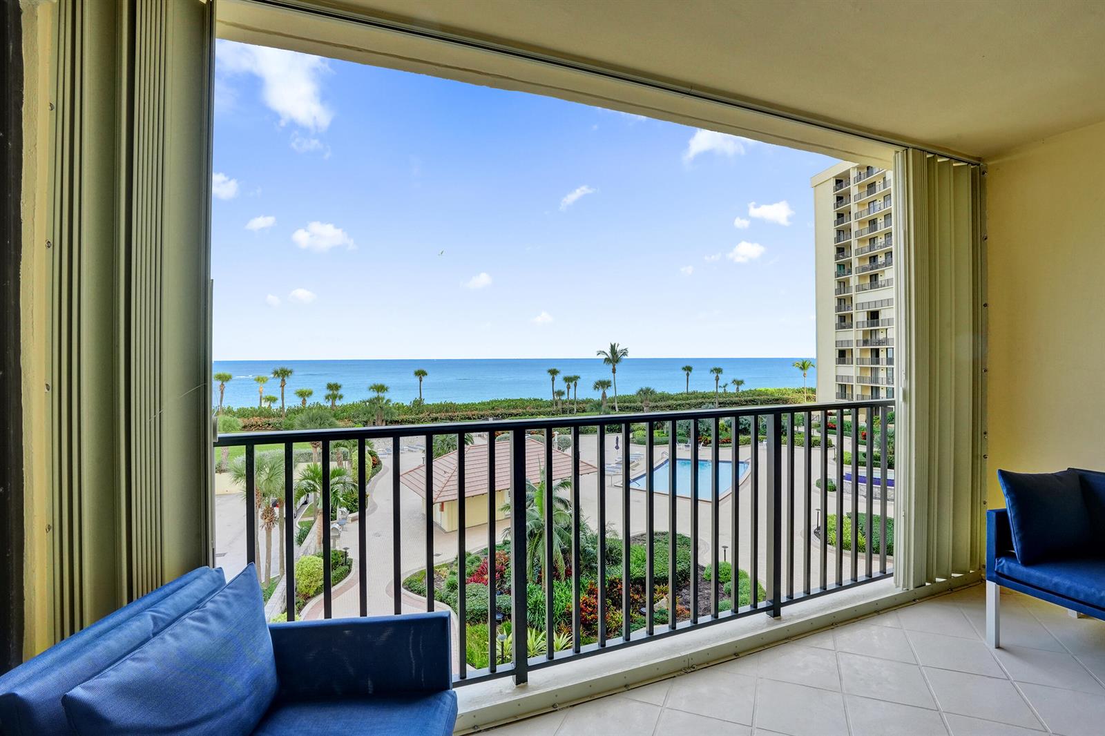 A balcony with blue seating overlooks a swimming pool, lush landscaping, and the ocean — 300 Ocean Trail Way # 410, Jupiter FL 33477, JUPITER, FL