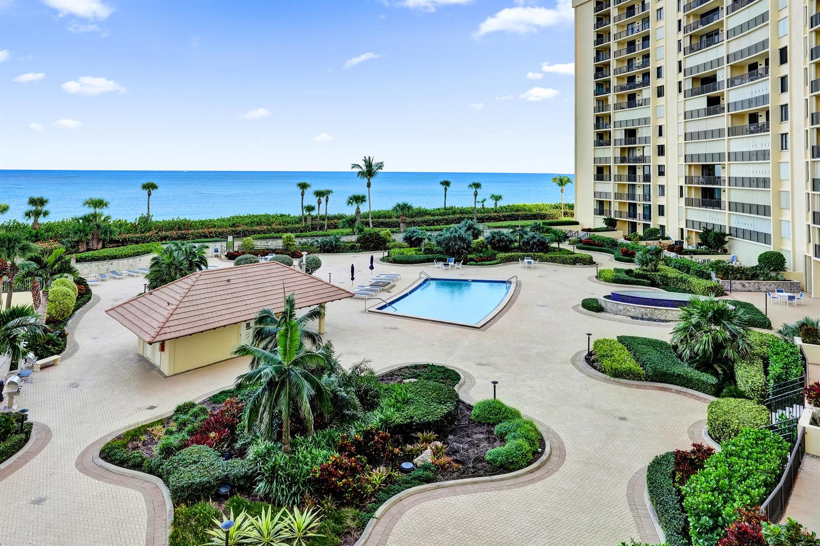 An elevated view of a swimming pool, patio, and landscaping beside a tall apartment building — 300 Ocean Trail Way # 410, Jupiter FL 33477, JUPITER, FL