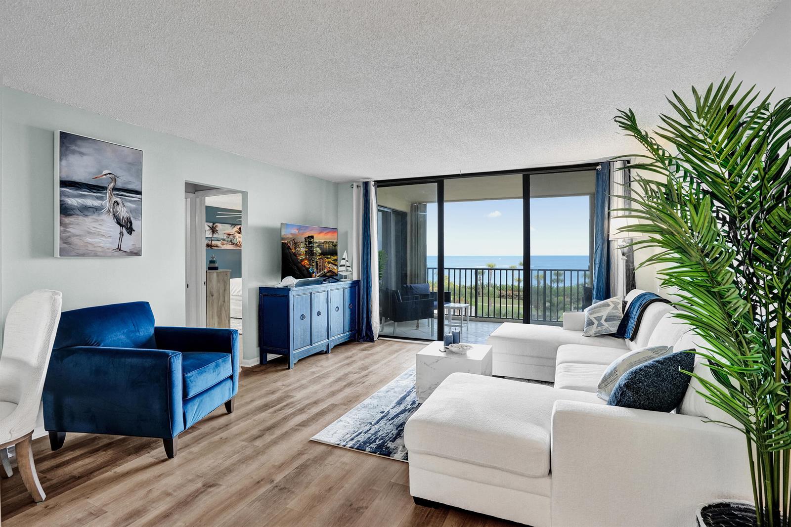 A living room features a white sectional, blue armchair, and sliding doors overlooking the ocean — 300 Ocean Trail Way # 410, Jupiter FL 33477, JUPITER, FL