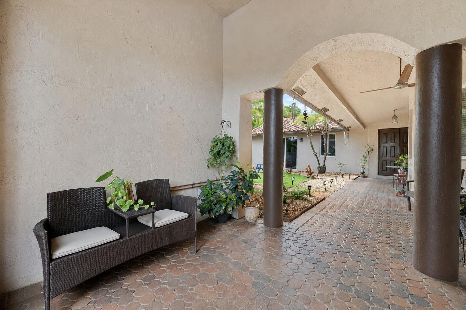 A covered patio features a wicker bench, potted plants, and brown columns on a paved floor — 14520 SW 37th Street, Miramar FL 33027, MIRAMAR, FL