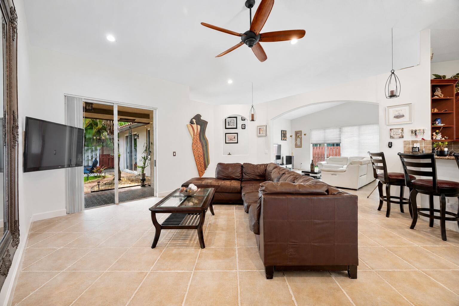 A living room with a brown sectional sofa, tile floors, and a sliding glass door — 14520 SW 37th Street, Miramar FL 33027, MIRAMAR, FL