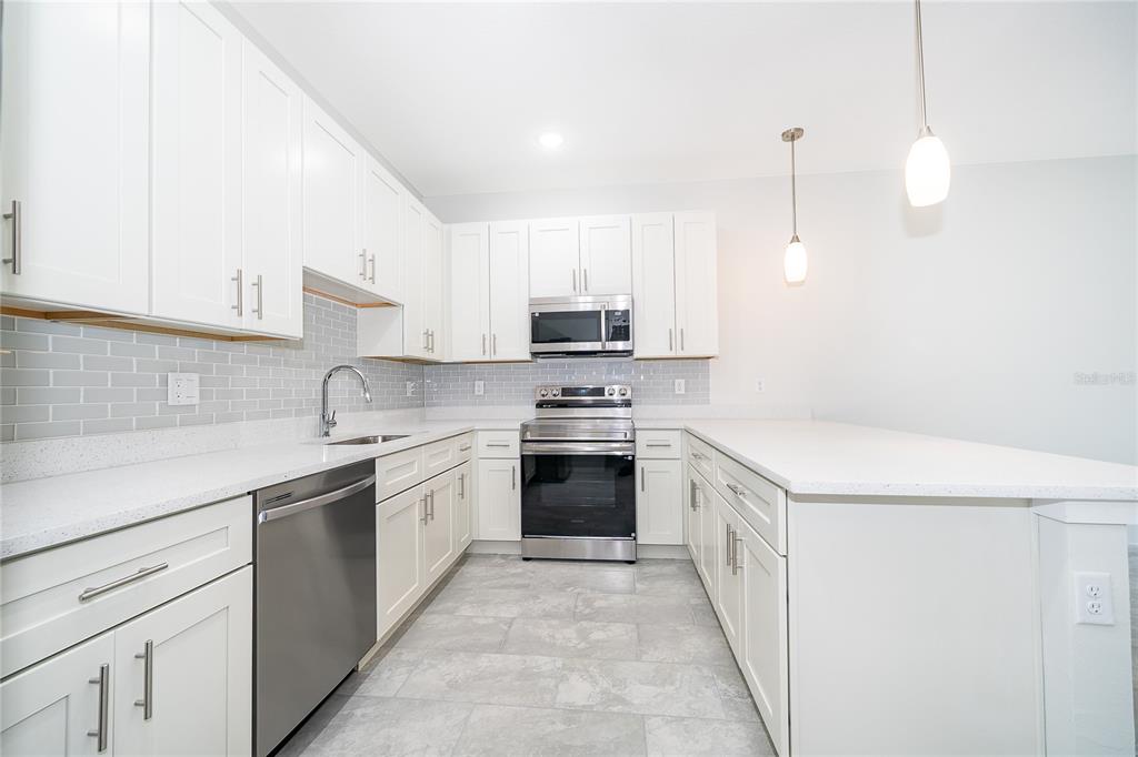 A modern kitchen features white cabinets, stainless steel appliances, a gray tile backsplash, and countertops — 1655 CUMIN DRIVE, KISSIMMEE, FL