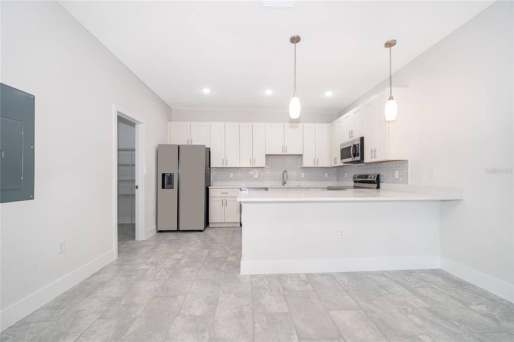 A modern kitchen features white cabinetry, stainless steel appliances, a breakfast bar, and tile flooring — 1655 CUMIN DRIVE, KISSIMMEE, FL