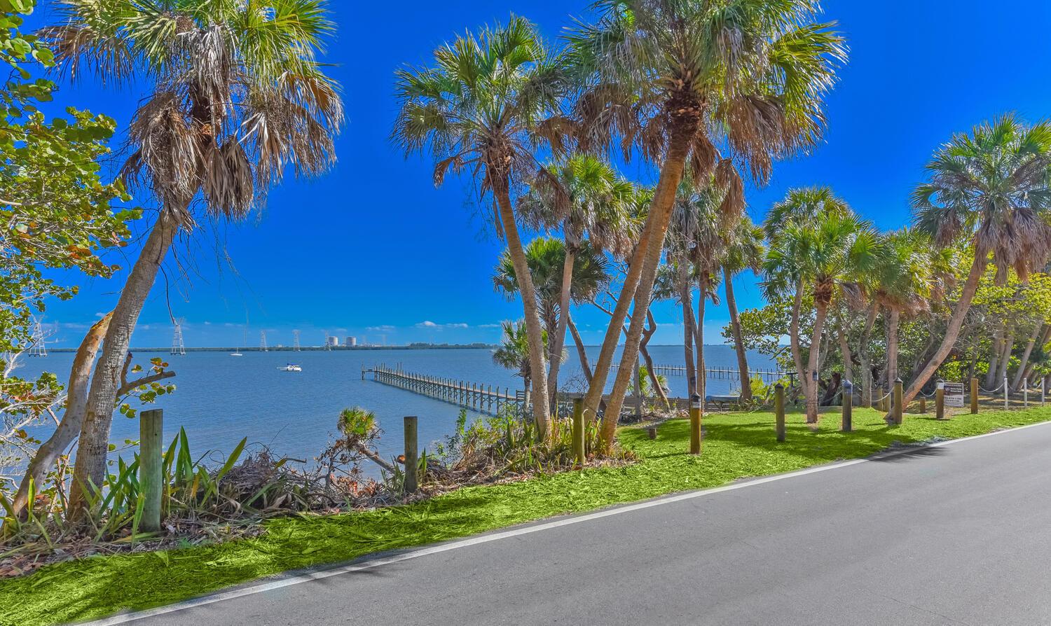 A paved road runs alongside a grassy area with palm trees overlooking a bay and pier — 8053 S Indian River Drive, Fort Pierce FL 34982, FORT PIERCE, FL