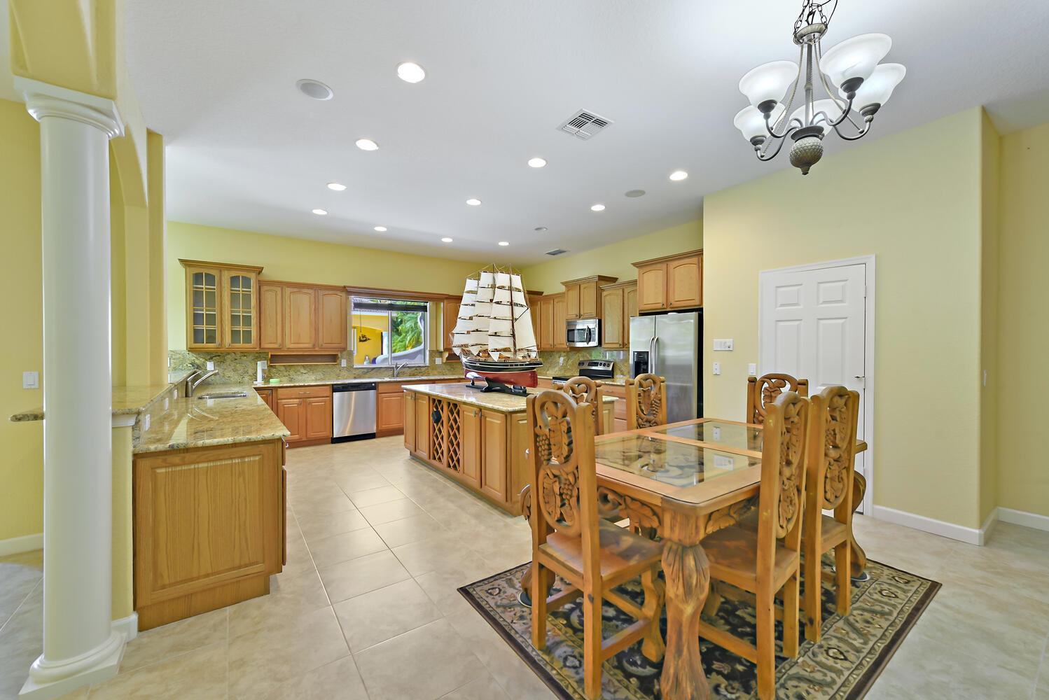 A kitchen with light wood cabinets, granite countertops, a central island, and a dining set — 8053 S Indian River Drive, Fort Pierce FL 34982, FORT PIERCE, FL