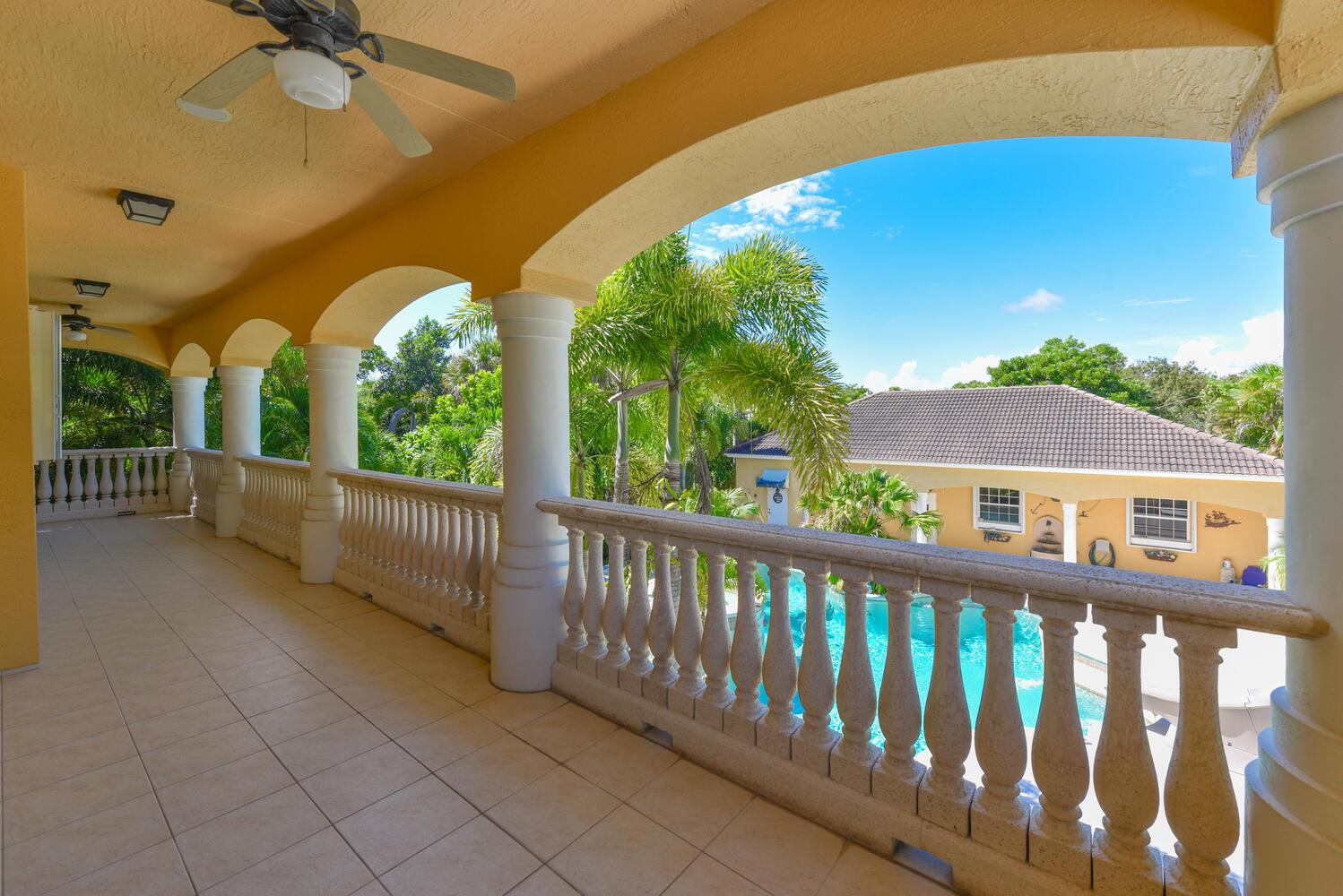 A covered balcony with stone balustrades overlooks a swimming pool and a neighboring house — 8053 S Indian River Drive, Fort Pierce FL 34982, FORT PIERCE, FL