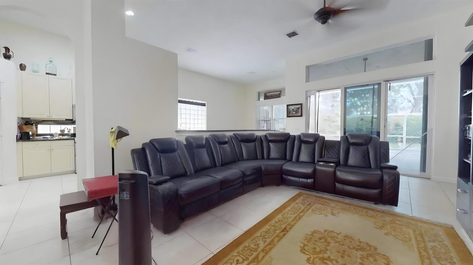 A living room features a large dark leather sectional sofa on a patterned area rug — 10072 Armani Drive, Boynton Beach FL 33437, BOYNTON BEACH, FL