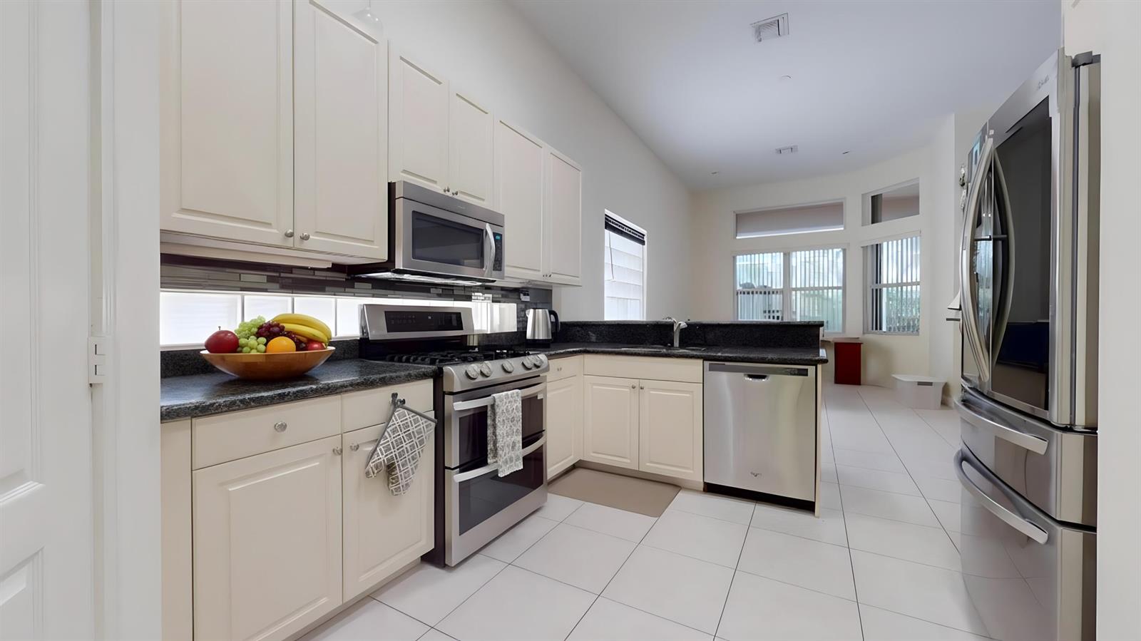 A kitchen features white cabinets, stainless steel appliances, dark countertops, and light tile flooring — 10072 Armani Drive, Boynton Beach FL 33437, BOYNTON BEACH, FL