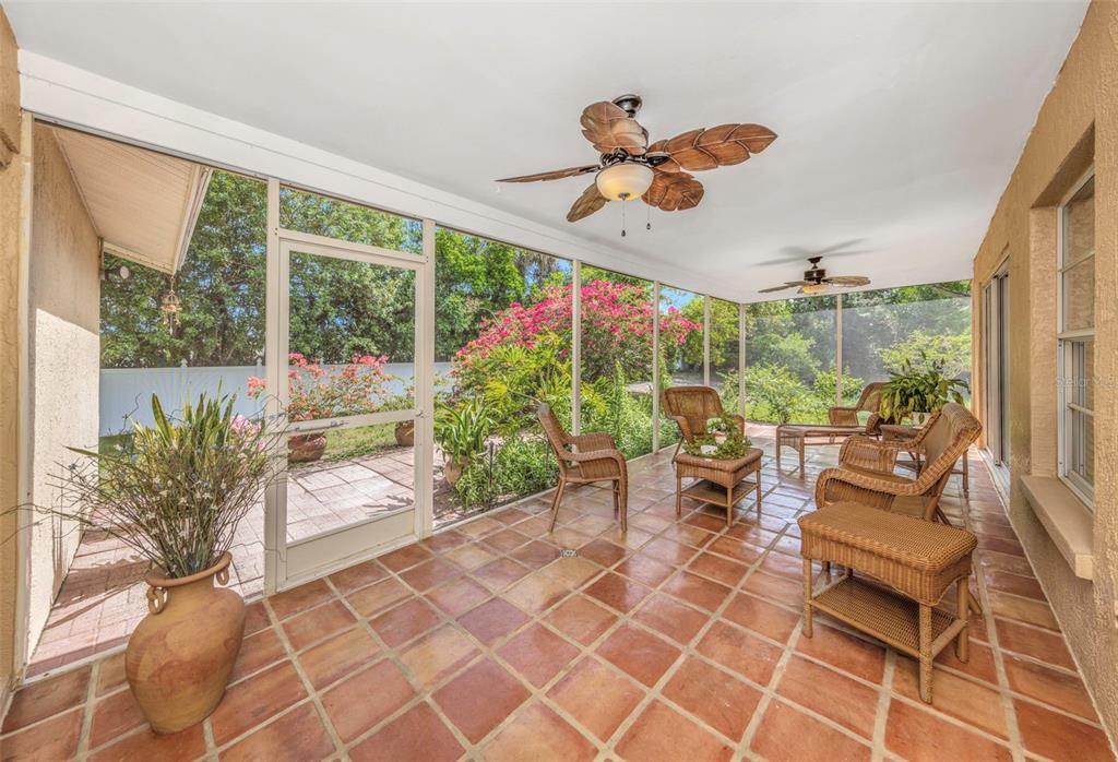 A screened-in patio features terracotta tile flooring, wicker furniture, and a ceiling fan — 2437 HAWK AVENUE, PALM HARBOR, FL