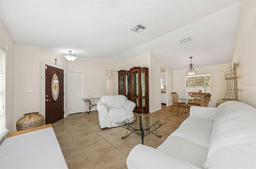 A living room with tile floors, white furniture, a glass coffee table, and a dining area — 2437 HAWK AVENUE, PALM HARBOR, FL
