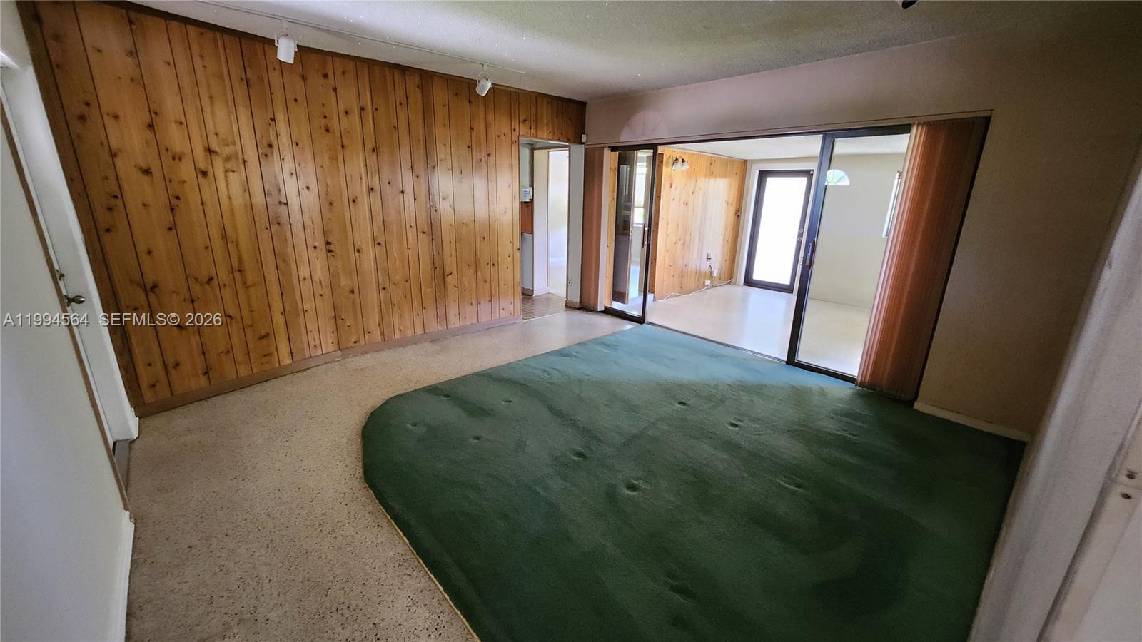 A room features wood-paneled walls, a green carpeted area, and sliding glass doors — 6241 NW 110th St, Hialeah FL 33012, HIALEAH, FL
