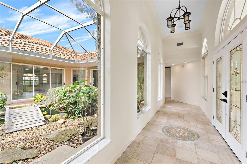 A bright hallway with tile floors overlooks an enclosed courtyard featuring a small wooden bridge — 8356 MAREVA LANE, SARASOTA, FL
