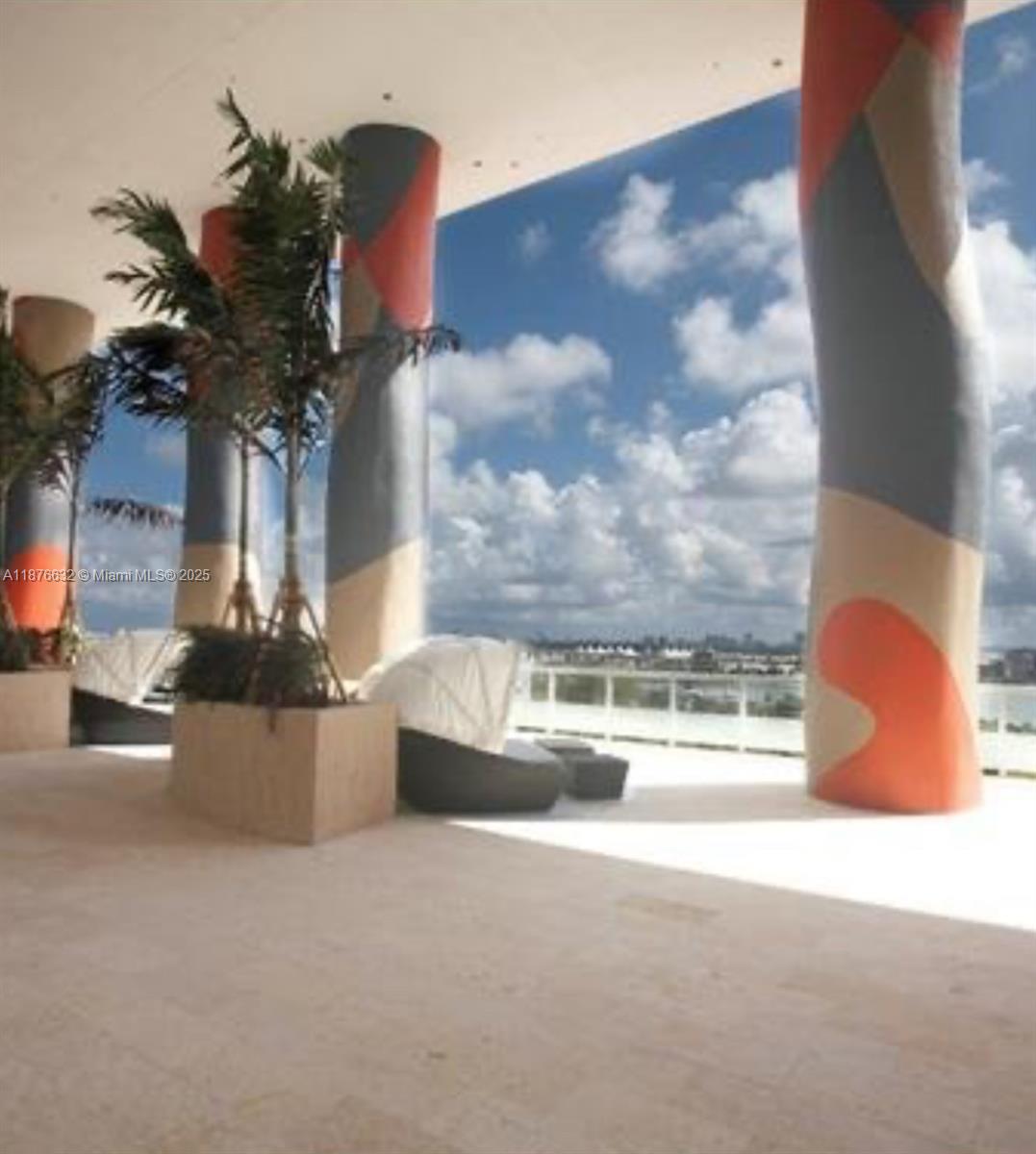 An outdoor terrace features large, patterned columns, potted palm trees, and lounge seating overlooking water — 50 Biscayne Blvd # 711, Miami FL 33132, MIAMI, FL