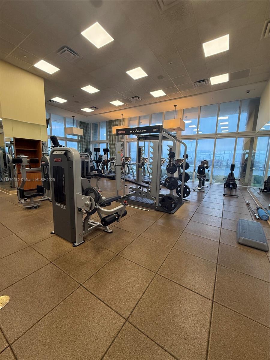 This fitness center features various exercise machines, a squat rack, and floor-to-ceiling windows — 50 Biscayne Blvd # 711, Miami FL 33132, MIAMI, FL