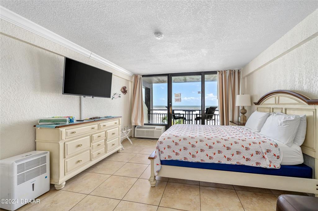 A bedroom with tile flooring, a queen bed, a dresser, and a balcony overlooking the ocean — 2301 S ATLANTIC AVENUE UNIT 236, DAYTONA BEACH, FL