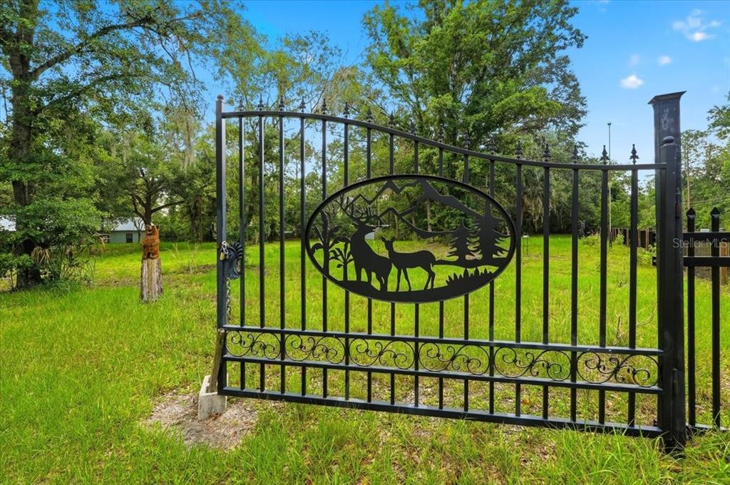 A black metal gate with a decorative deer and mountain cutout stands in a grassy field — 1425 PIONEER DRIVE, LAKELAND, FL