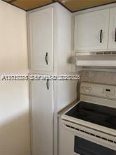 A white kitchen cabinet pantry stands next to a white electric stove and range hood — 3774 Inverrary Blvd # 305P, Lauderhill FL 33319, LAUDERHILL, FL