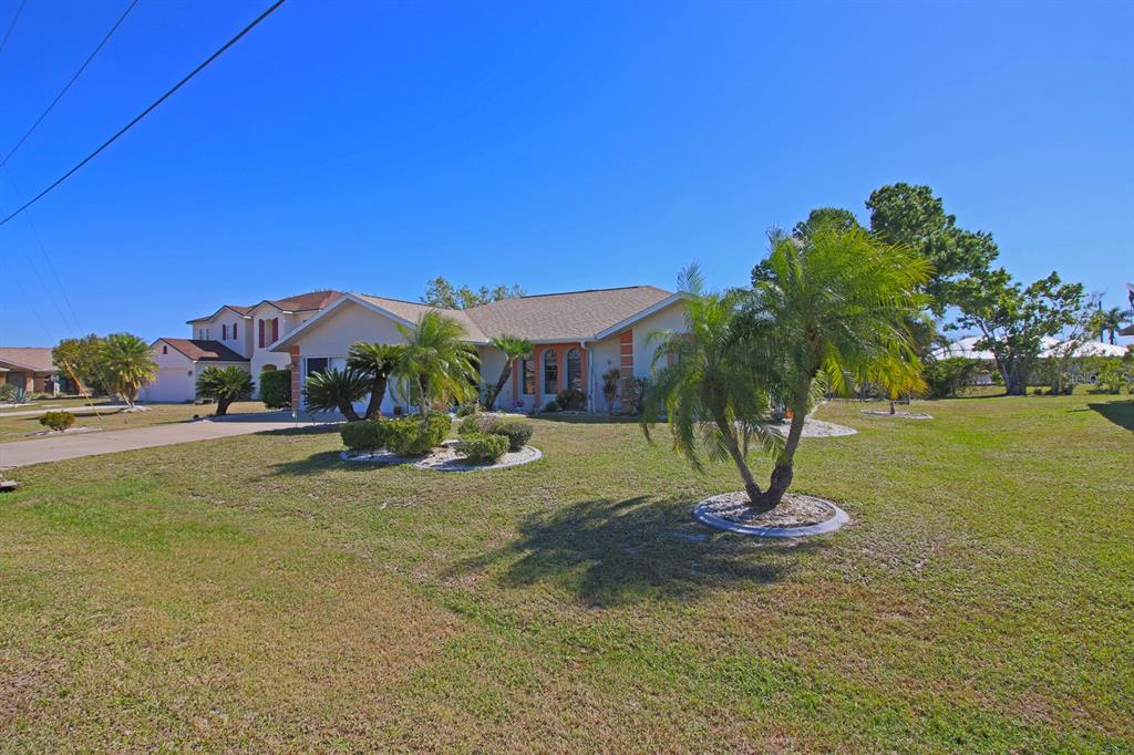 A single-story house with a tan exterior, a shingled roof, and palm trees in the yard — 32 BARILOCHE DRIVE, PUNTA GORDA, FL