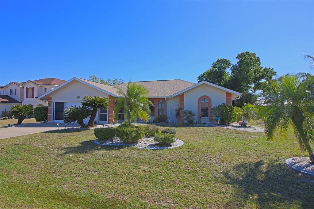 A single-story house with a tan exterior, orange trim, and a landscaped front yard — 32 BARILOCHE DRIVE, PUNTA GORDA, FL