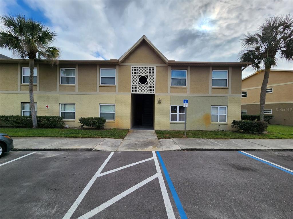 A two-story apartment building exterior features tan stucco walls, a central entryway, and palm trees — 9933 SWEEPSTAKES LANE UNIT 6, ORLANDO, FL