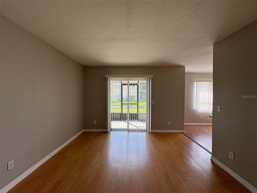 An empty room with light wood-look flooring, beige walls, and a sliding glass door — 9933 SWEEPSTAKES LANE UNIT 6, ORLANDO, FL