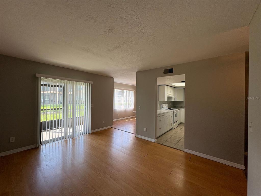 A living room with wood-look flooring leads to a kitchen and a sliding glass door — 9933 SWEEPSTAKES LANE UNIT 6, ORLANDO, FL