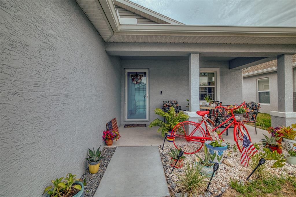 A covered front porch features a red decorative bicycle, potted plants, and a glass door — 10541 S DREW BRYANT CIRCLE, FLORAL CITY, FL