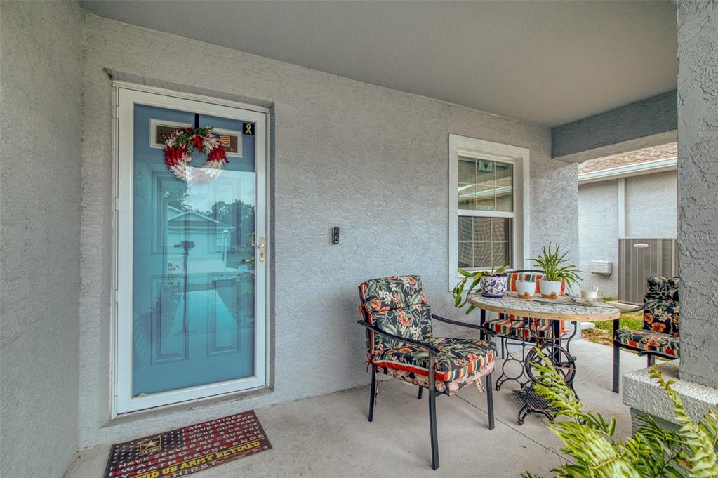 A covered front porch features a blue storm door, a small bistro set, and a doormat — 10541 S DREW BRYANT CIRCLE, FLORAL CITY, FL