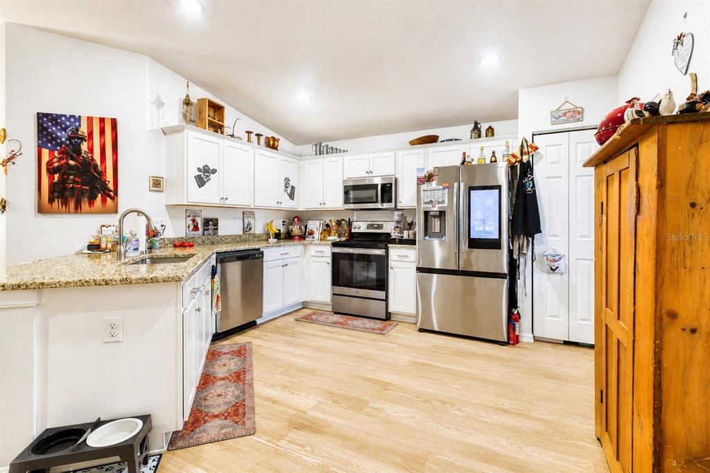 A kitchen features white cabinets, granite countertops, stainless steel appliances, and light wood flooring — 10541 S DREW BRYANT CIRCLE, FLORAL CITY, FL