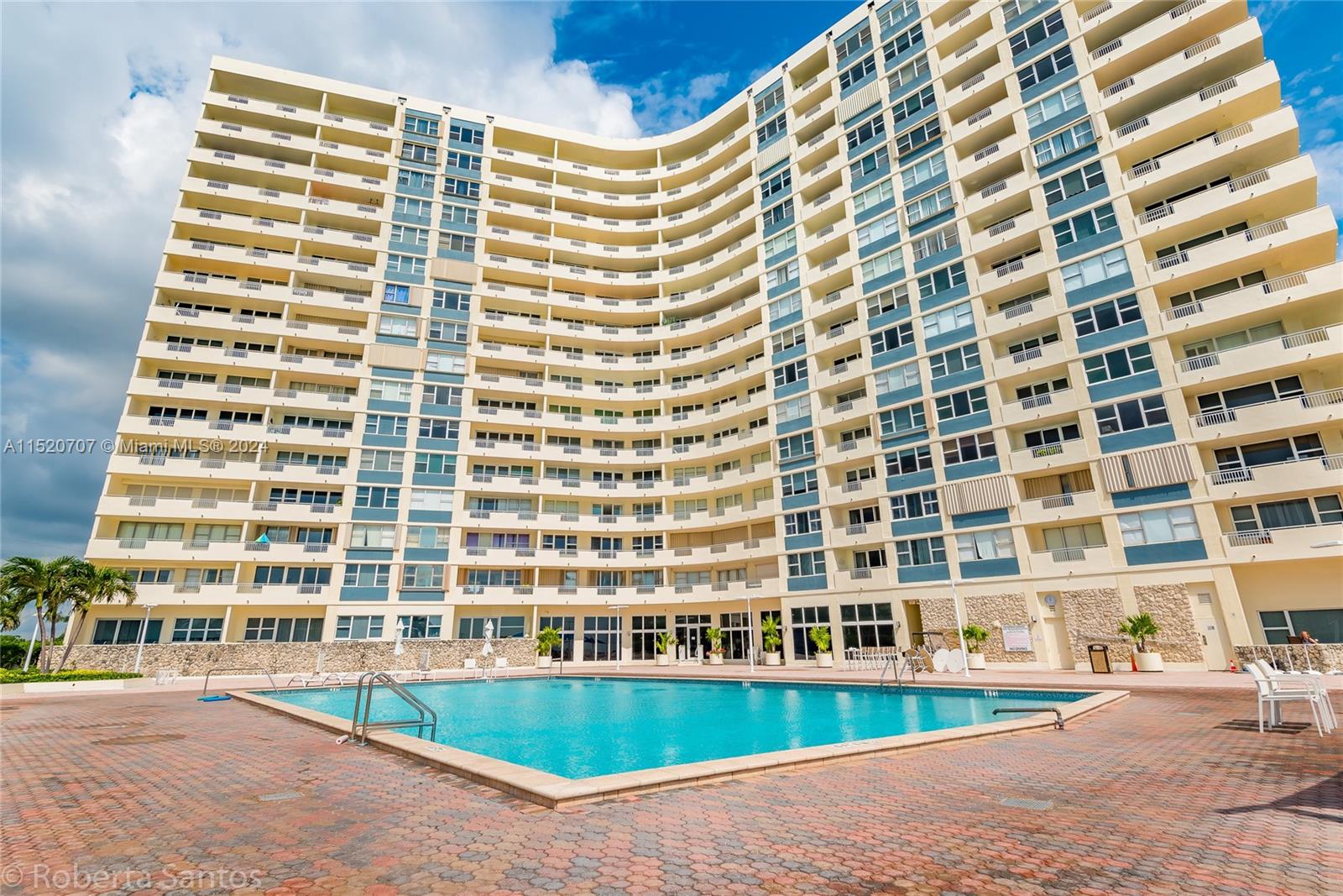 A large, curved apartment building stands behind a rectangular swimming pool on a paved deck — 3180 S Ocean Dr # 422, Hallandale Beach FL 33009, HALLANDALE BEACH, FL
