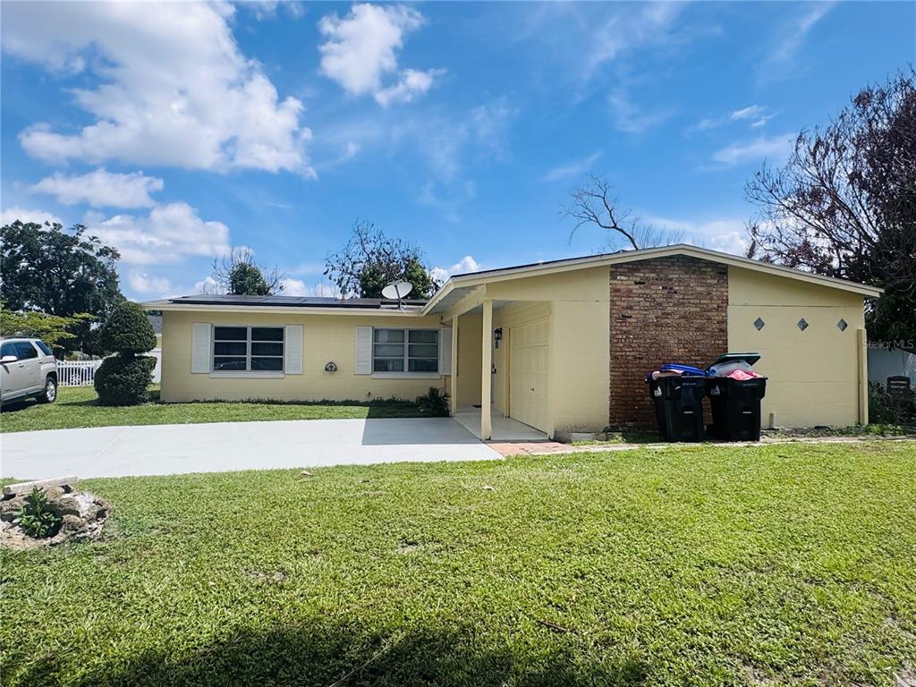 A yellow single-story house features a brick accent wall and a concrete driveway — 767 FORESTER AVENUE, ORLANDO, FL
