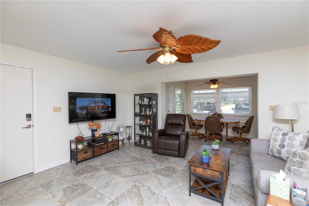 A living room with tile floors, a ceiling fan, a television, and an adjacent dining area — 4812 JASPER DRIVE UNIT 107, NEW PORT RICHEY, FL