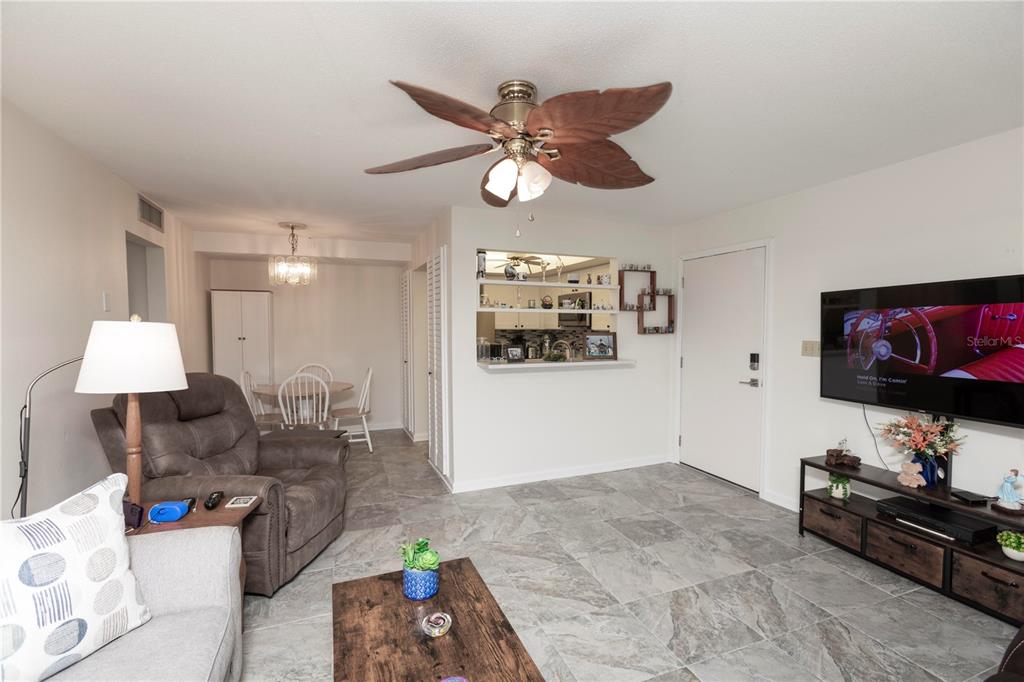 A living room with gray tile flooring, a ceiling fan, and an open kitchen pass-through — 4812 JASPER DRIVE UNIT 107, NEW PORT RICHEY, FL