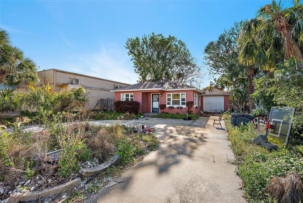 A single-story pink house with a concrete driveway and overgrown landscaping under a blue sky — 420 77TH AVENUE, ST PETE BEACH, FL