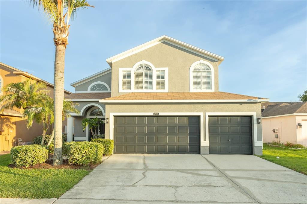 A two-story suburban house features a three-car garage, a concrete driveway, and a palm tree — 27506 WAIKIKI COURT, WESLEY CHAPEL, FL