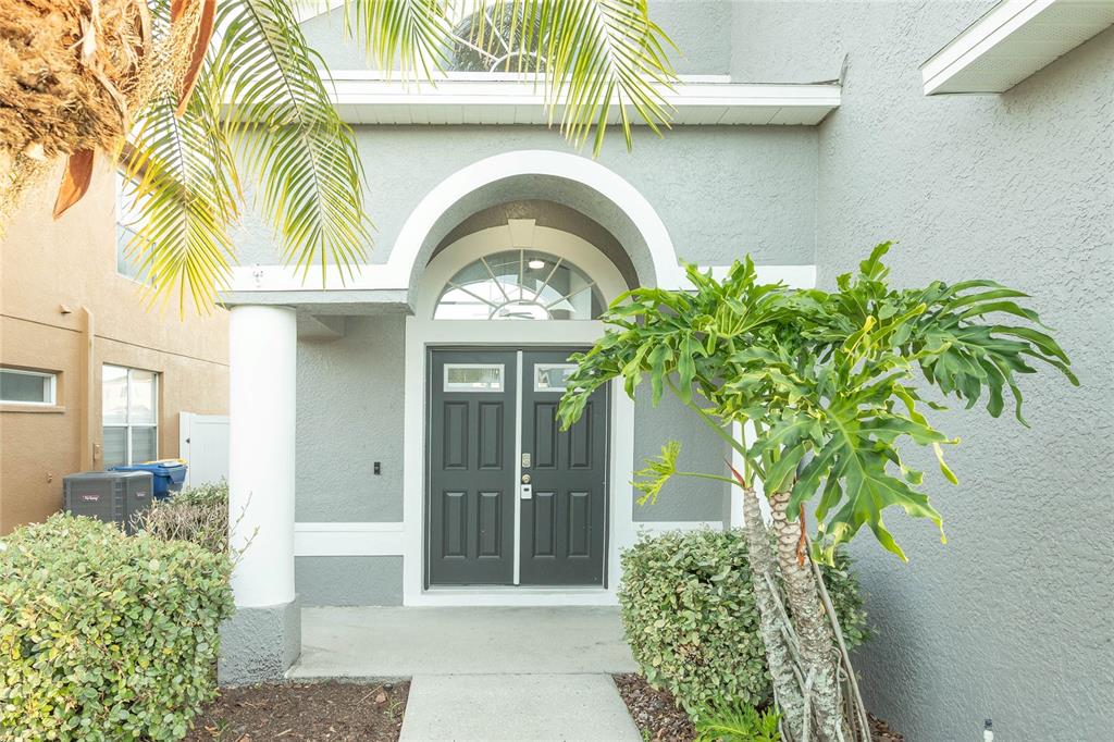 The exterior of a house features a gray facade, a white arched entryway, and double doors — 27506 WAIKIKI COURT, WESLEY CHAPEL, FL