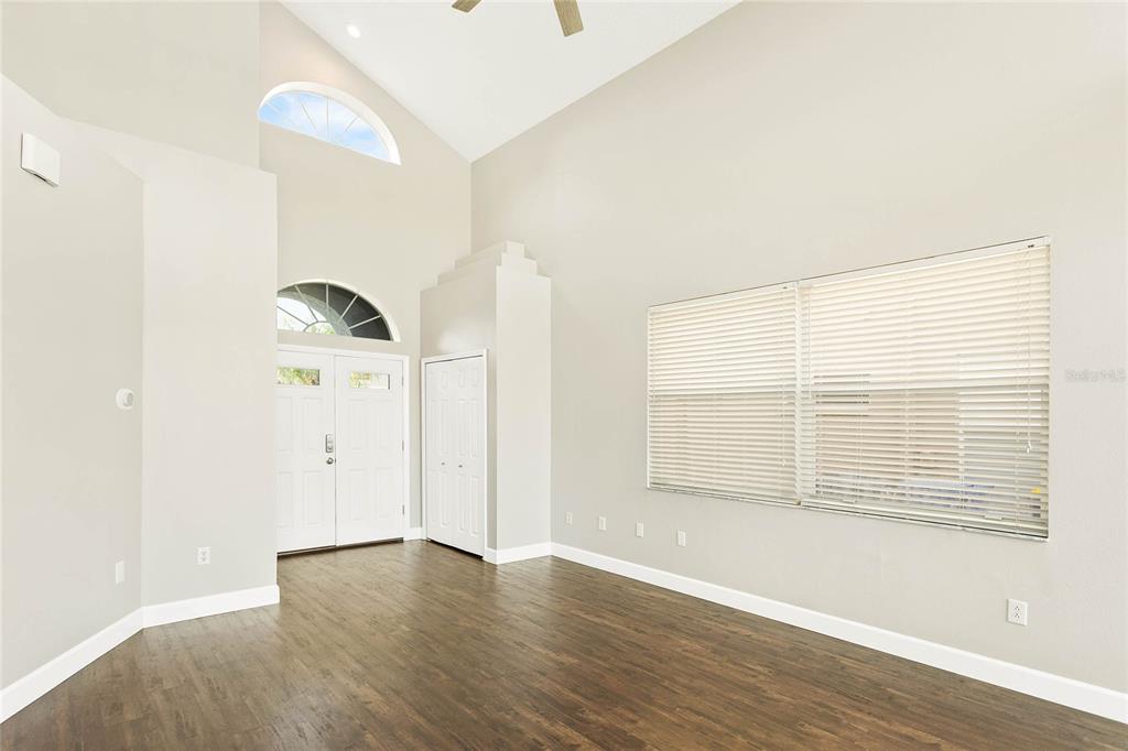 An empty room with high ceilings, dark wood floors, a double door, and large windows — 27506 WAIKIKI COURT, WESLEY CHAPEL, FL