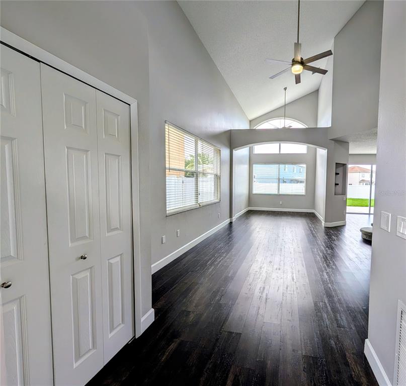 A living room with dark wood flooring, vaulted ceilings, a ceiling fan, and white doors — 27506 WAIKIKI COURT, WESLEY CHAPEL, FL