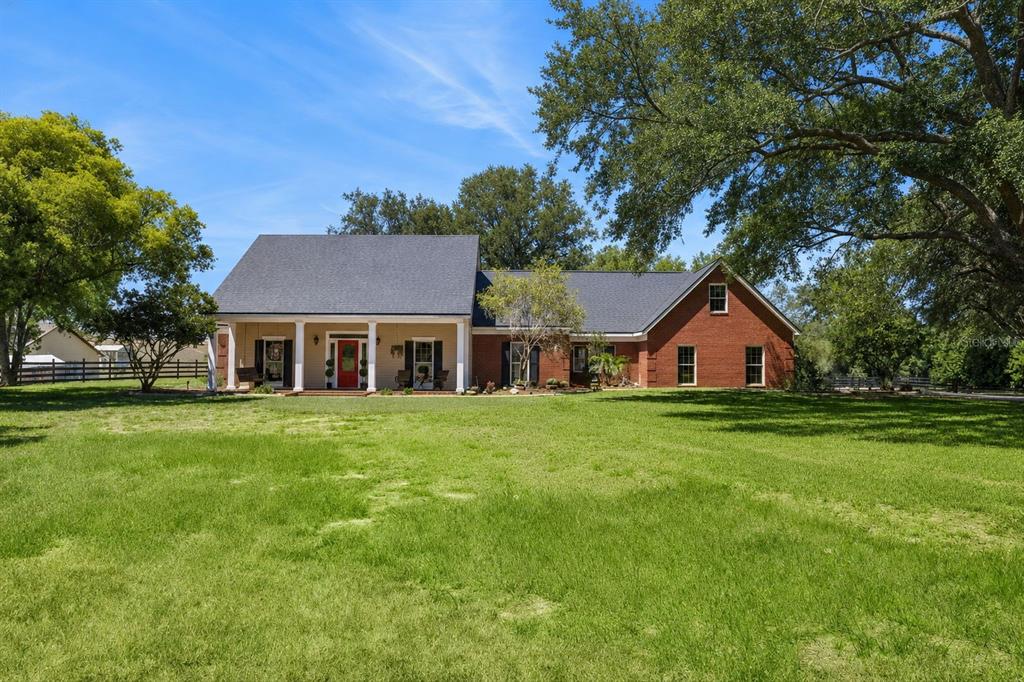A covered brick porch features a ceiling fan, two chairs, and a topiary plant — 14951 THOROUGHBRED LN, MONTVERDE, FL