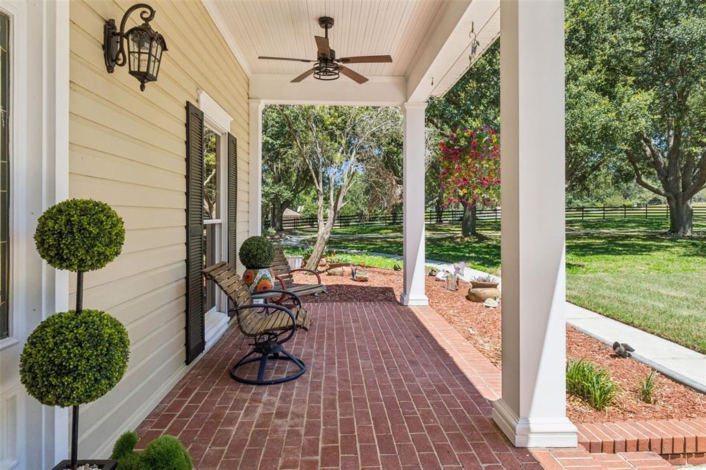 A covered brick porch features a ceiling fan, hanging swing, and outdoor seating — 14951 THOROUGHBRED LN, MONTVERDE, FL
