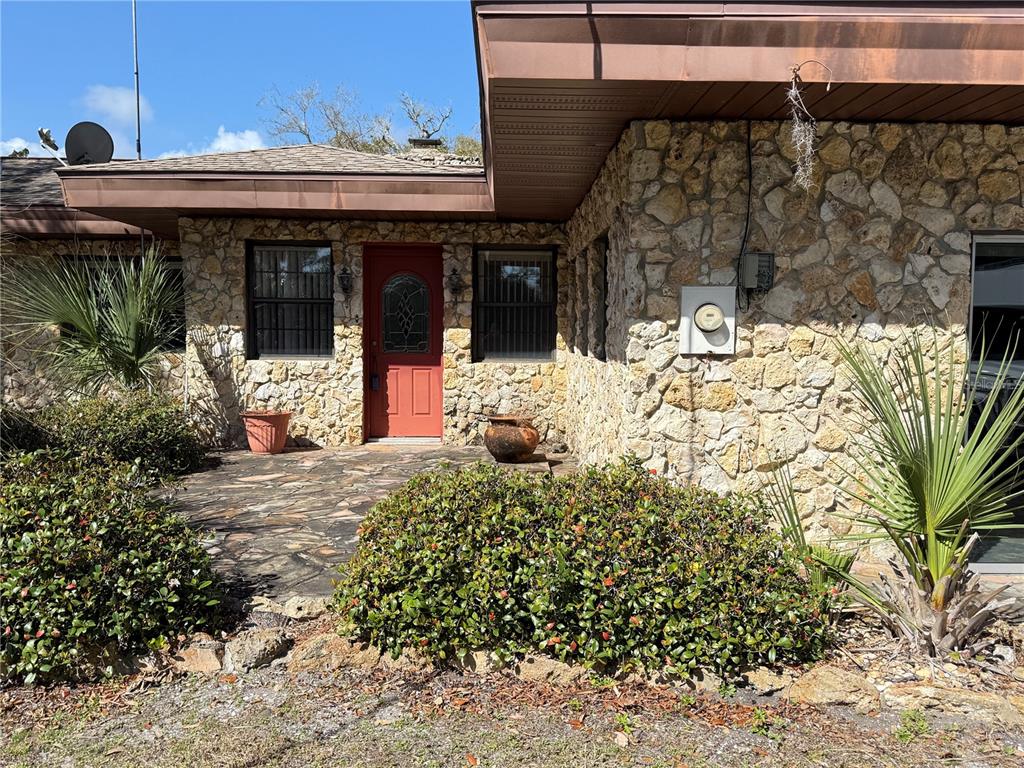 The exterior of a stone house features a red front door and a paved patio — 508 S INDIAN RIVER ROAD, NEW SMYRNA BEACH, FL