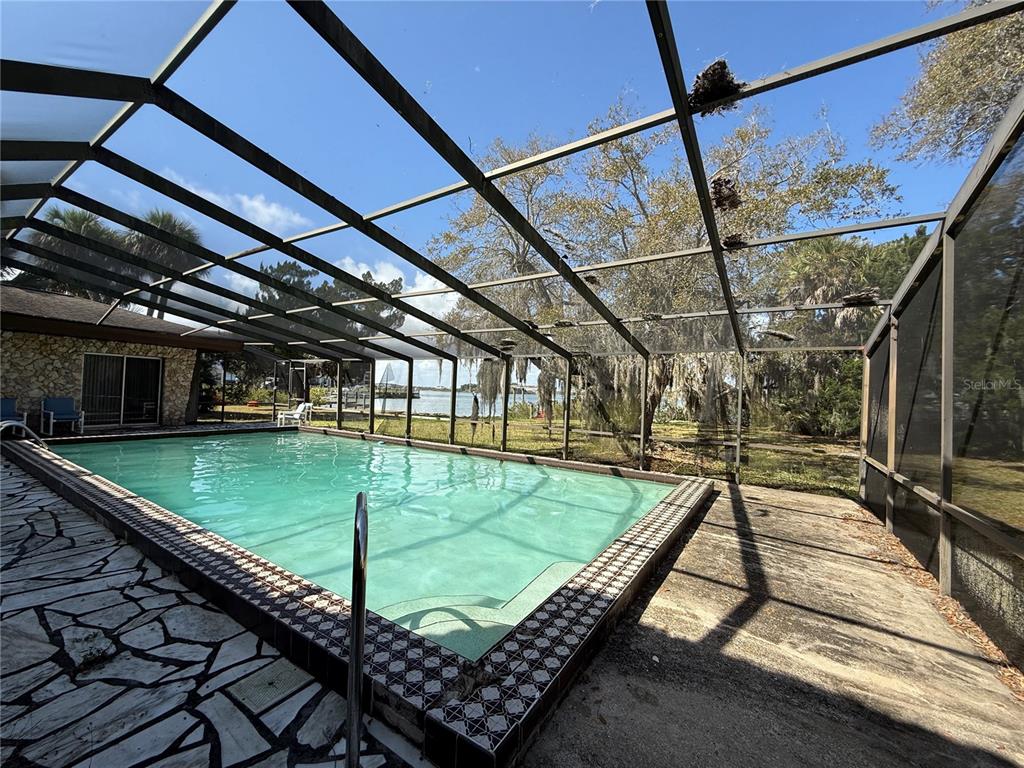 A screened-in swimming pool with a stone patio overlooks a body of water — 508 S INDIAN RIVER ROAD, NEW SMYRNA BEACH, FL