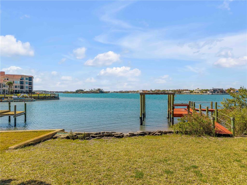 A grassy yard overlooks a calm bay with a wooden dock and distant waterfront homes — 508 S INDIAN RIVER ROAD, NEW SMYRNA BEACH, FL